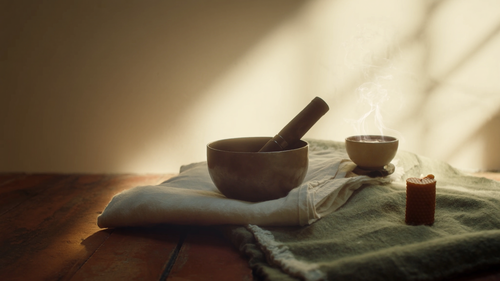 Stillleben: Messing-Klangschale, Decke aus Leinen und Wolle, Tasse Kakao mit aufsteigendem Dampf, Bienenwachs-Kerze, warmes Morgenlicht auf Holzboden.